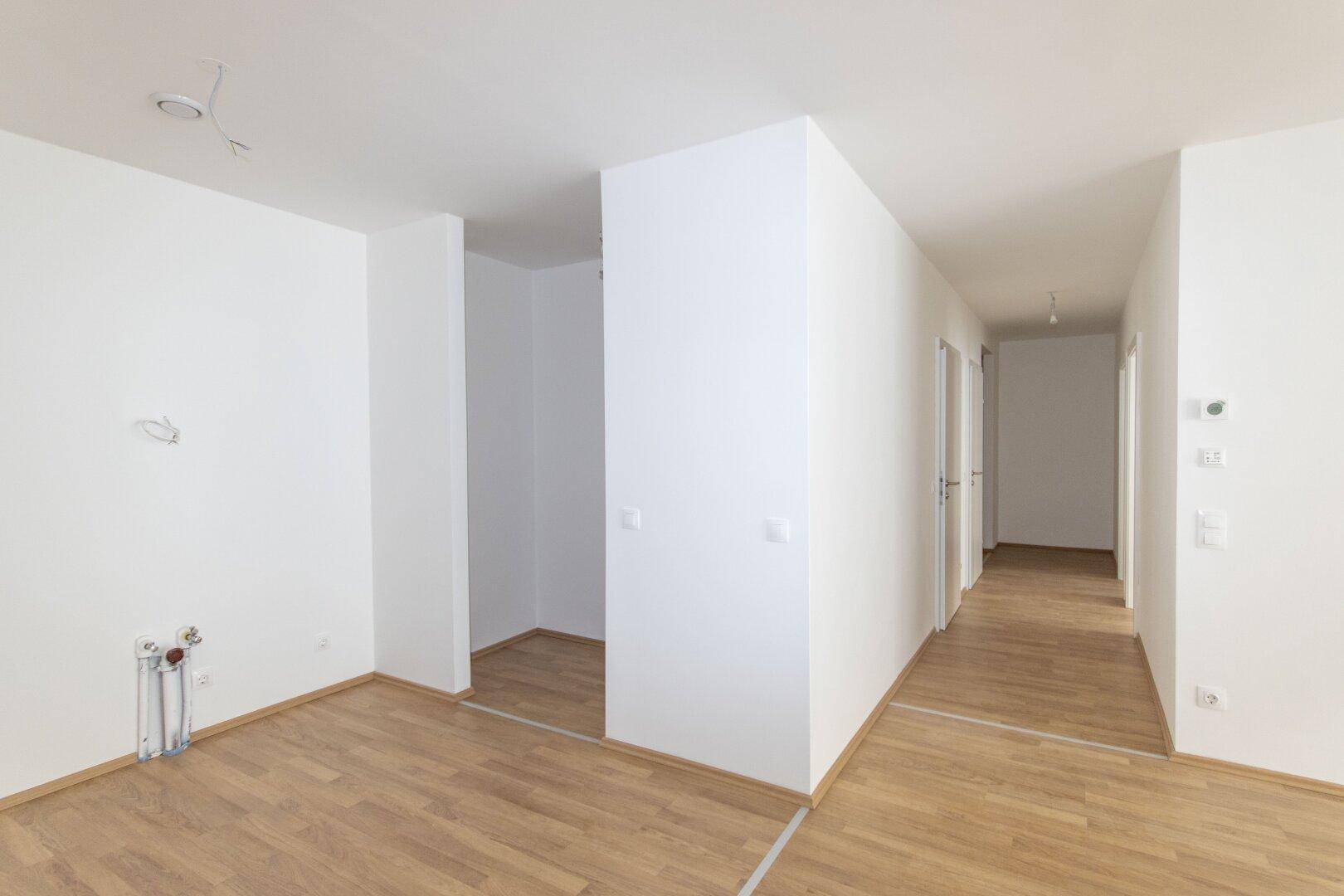 Heller Eingangsbereich mit Laminatboden, der in einen langen Flur mit mehreren Türen führt.
