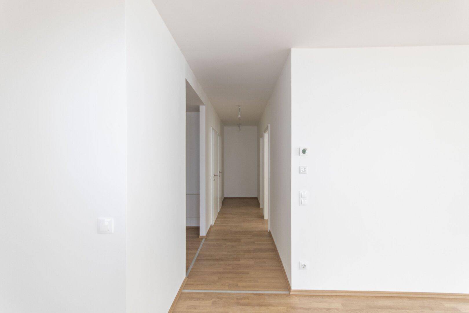 Langer, heller Flur mit Holzboden und weißen Wänden, der die Wohnbereiche verbindet.