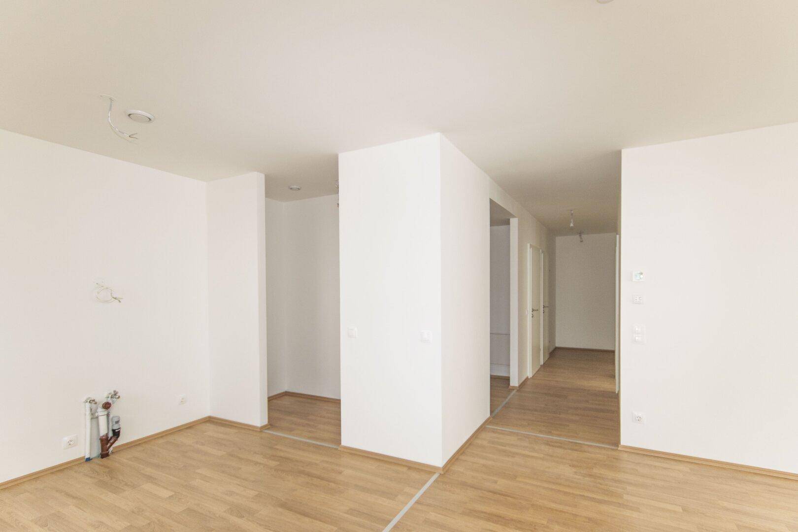 Heller Flur mit Holzboden und weißen Wänden, der zu weiteren Räumen führt.