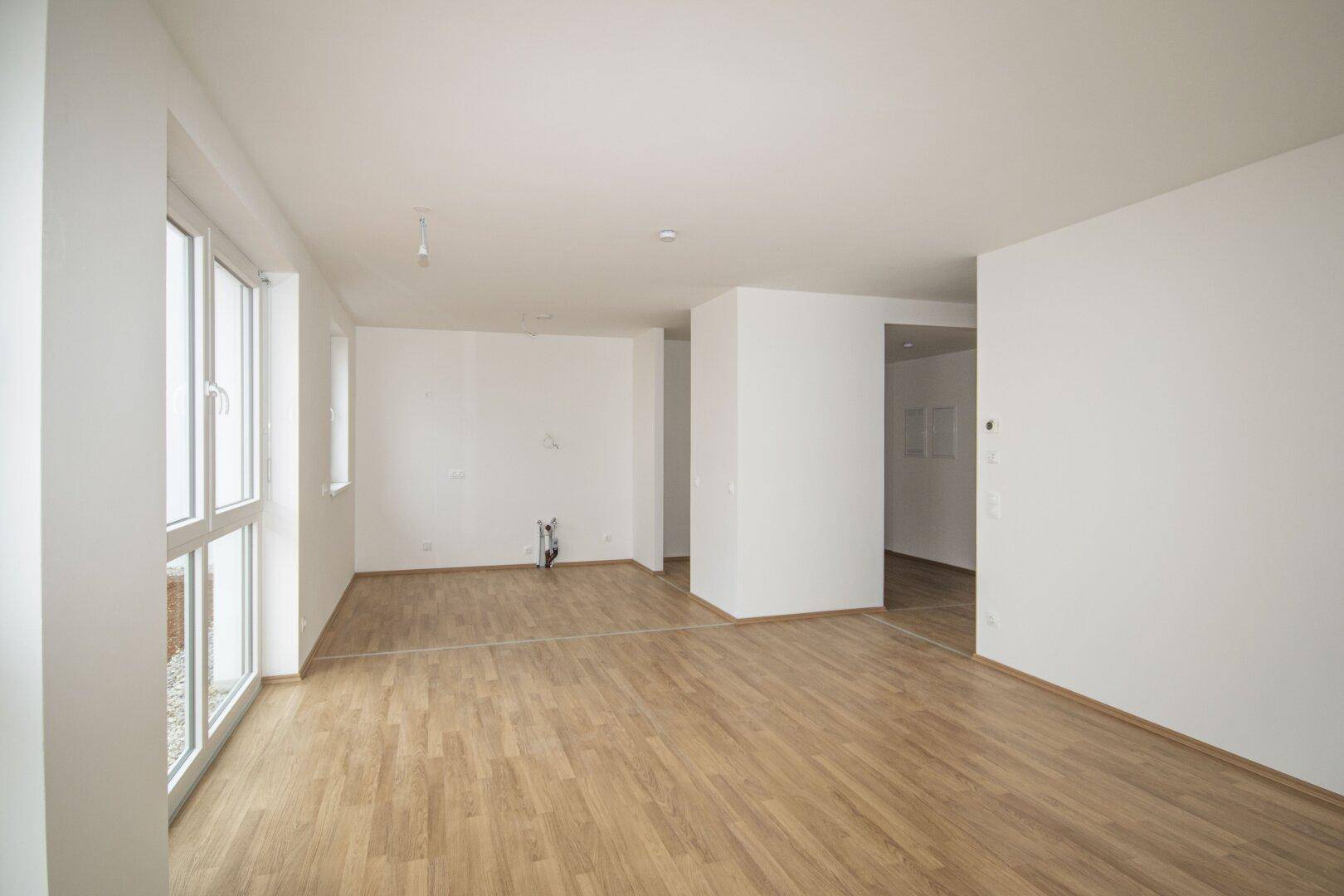 Geräumiger, heller Innenraum mit Holzboden und weiß gestrichenen Wänden, ideal für offenes Wohnen.