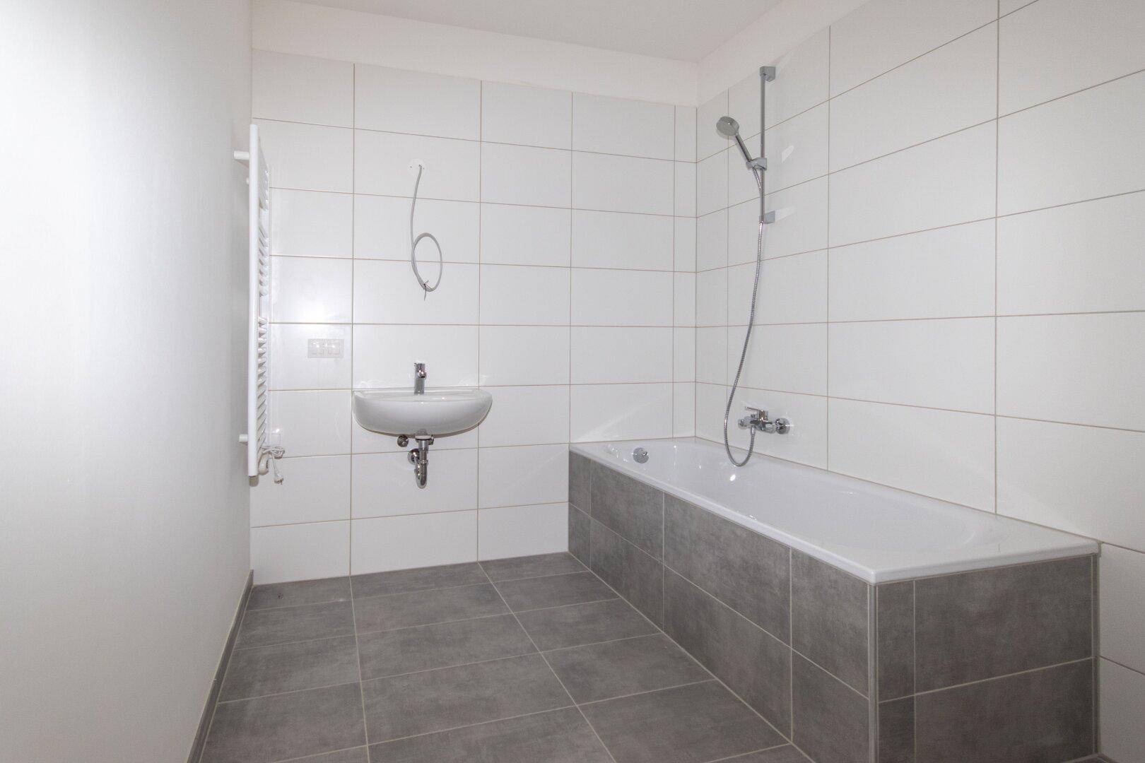 Modernes Badezimmer mit Badewanne, Waschbecken und weißen sowie grauen Fliesen.