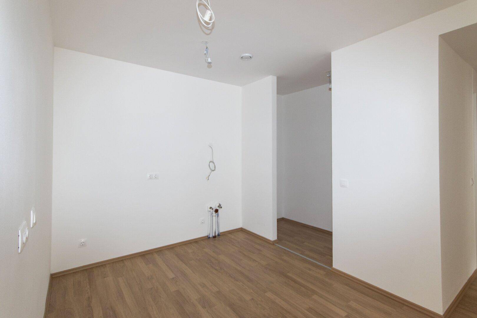 Leerer Raum mit Laminatboden und Anschlüssen für eine Küche, bereit zum Einbau.