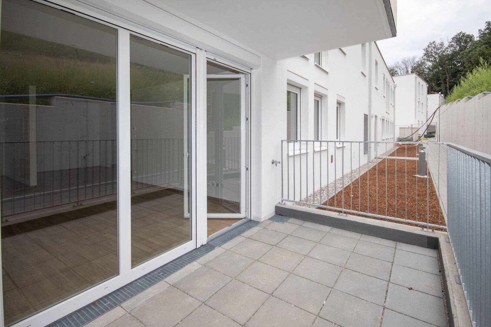 Geräumige Terrasse im Erdgeschoss mit Fliesenboden und Zugang zum Gartenbereich der Wohnanlage.