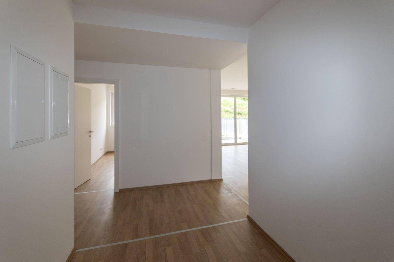 Geräumiger Flur mit Laminatboden und weißen Wänden, der viel Tageslicht in den Wohnbereich leitet.