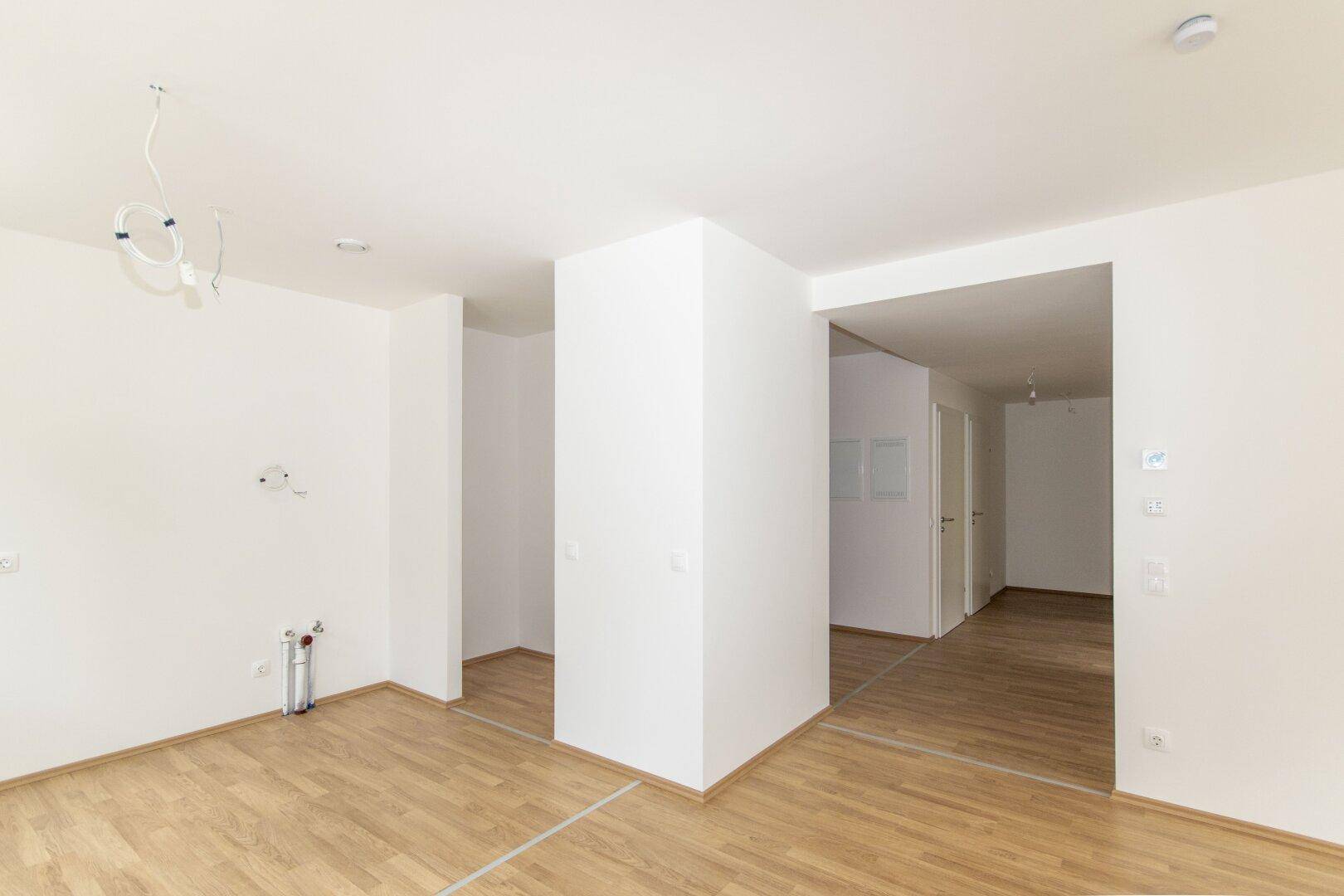 Heller Flur mit Laminatboden und weißen Wänden, der zu weiteren Räumen führt.