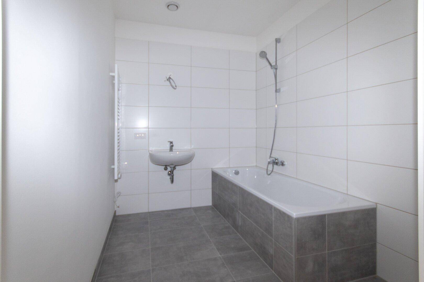 Modernes Badezimmer mit weißen Fliesen, Badewanne, Einzelwaschbecken und beheiztem Handtuchhalter.