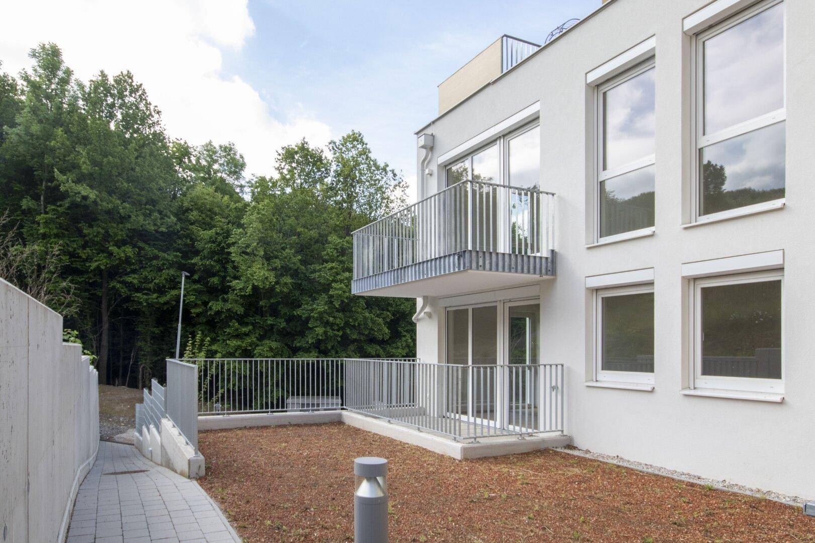 Moderne Gebäudefassade mit Balkonen und einer ebenerdigen Terrasse mit Blick ins Grüne.