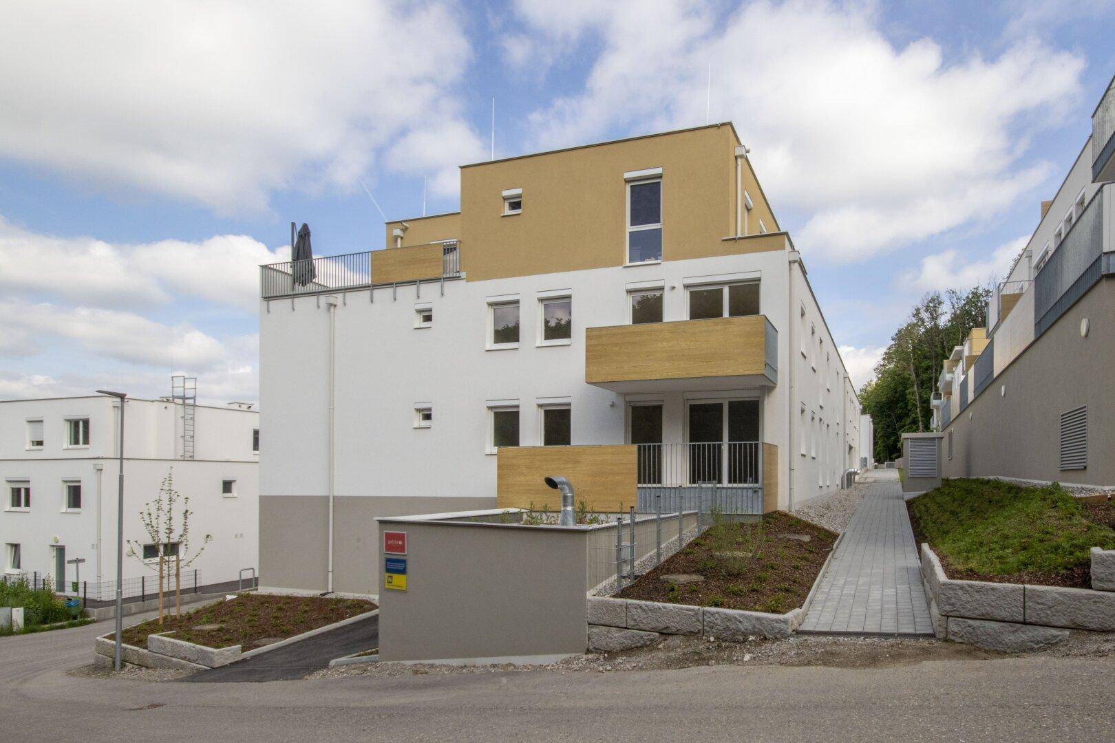 Modernes Mehrfamilienhaus mit weißer und gelber Fassade in einer grünen Umgebung.