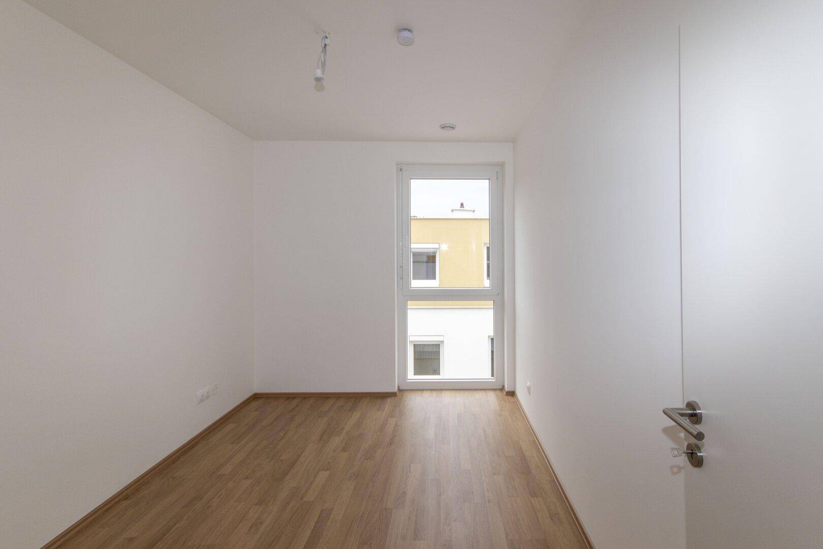 Kleiner, heller Raum mit Laminatboden und einem Fenster, ideal als Schlaf- oder Arbeitszimmer.