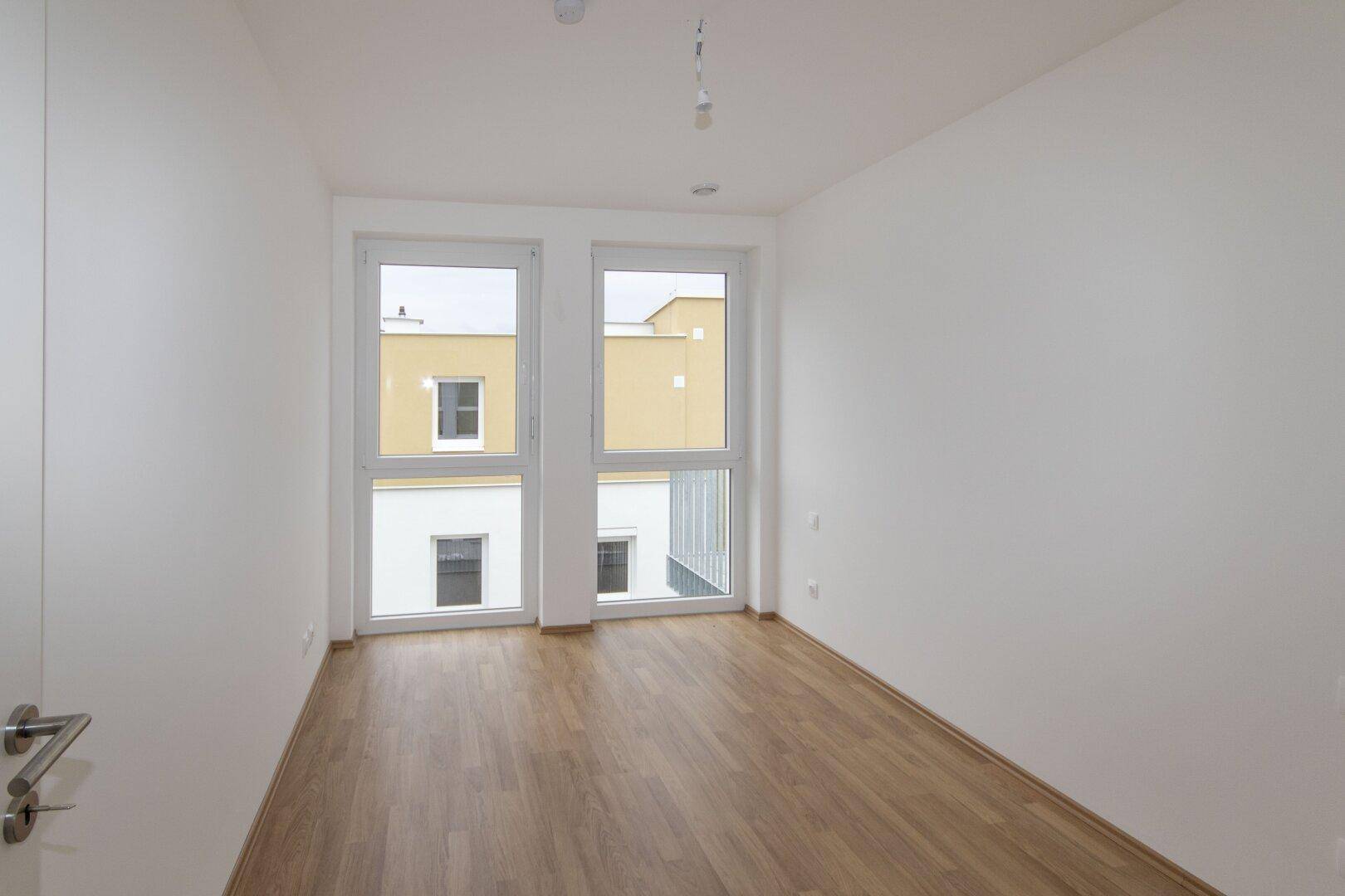 Heller Raum mit Laminatboden und zwei Fenstern, bietet viel Tageslicht und Flexibilität.