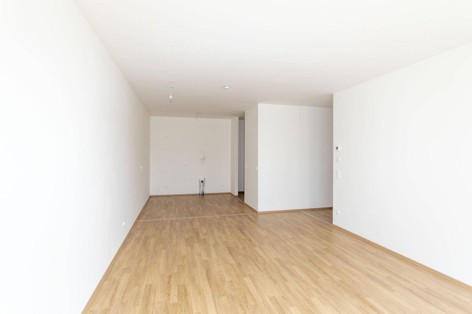 Geräumiger, leerer Raum mit hellem Laminatboden und weißen Wänden, bereit zur Gestaltung.