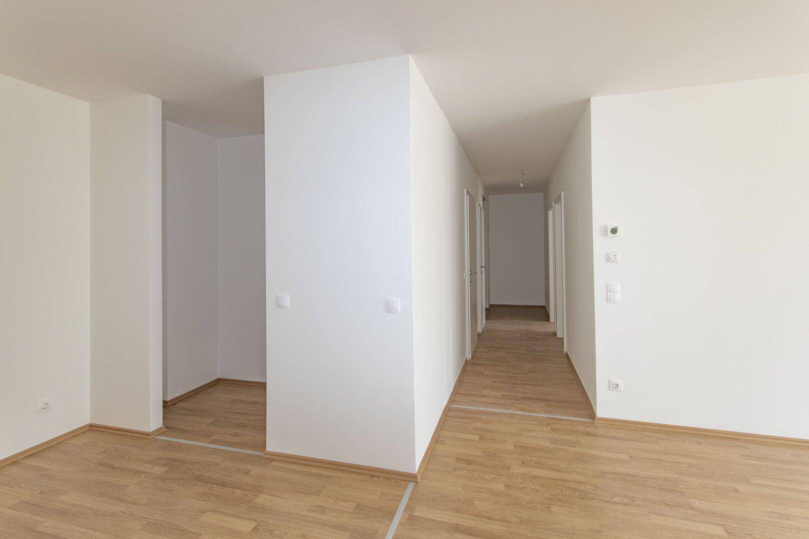 Heller Flur mit Laminatboden und weißen Wänden, der zu verschiedenen Räumen führt.