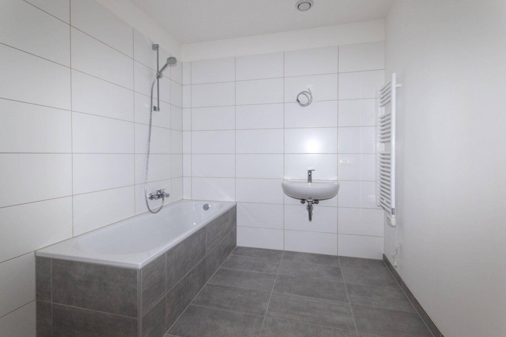 Modernes Badezimmer mit Badewanne, Waschbecken und hellgrauen Fliesen.