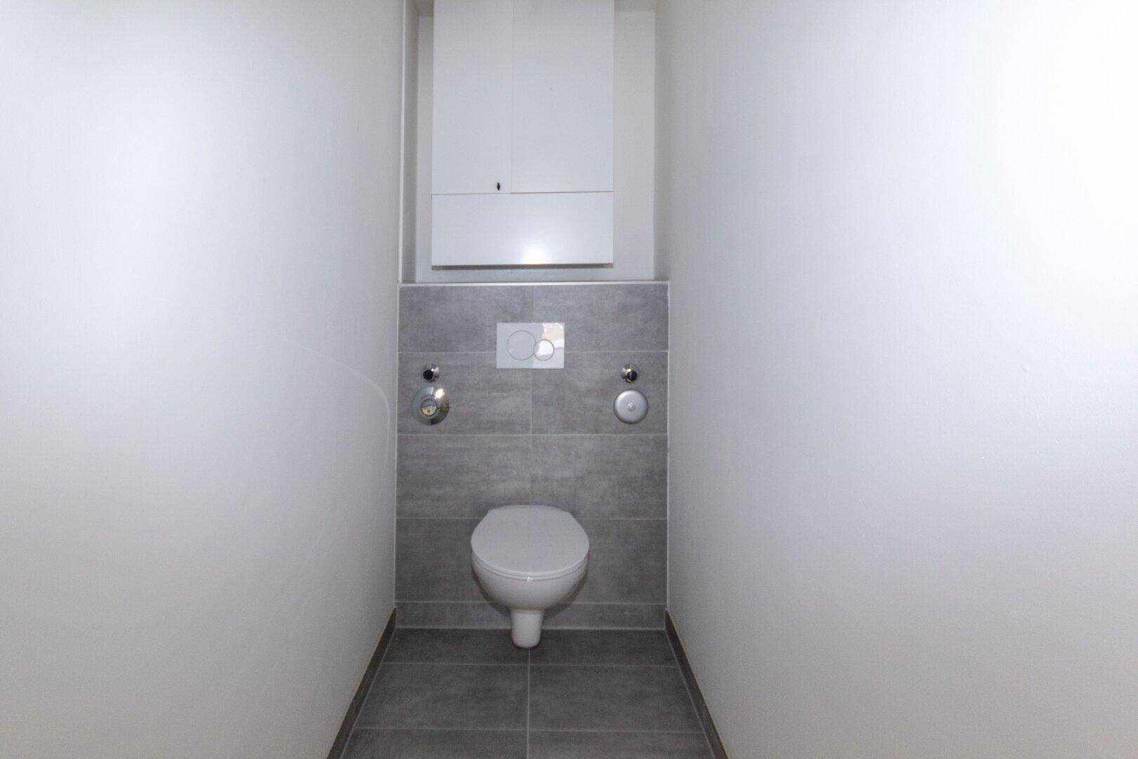 Separates WC mit wandhängender Toilette und modernen grauen Fliesen.