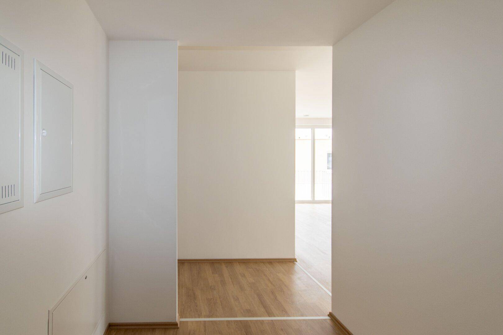 Eingangsbereich mit Laminatboden und weißen Wänden, der in den offenen Wohnbereich übergeht.