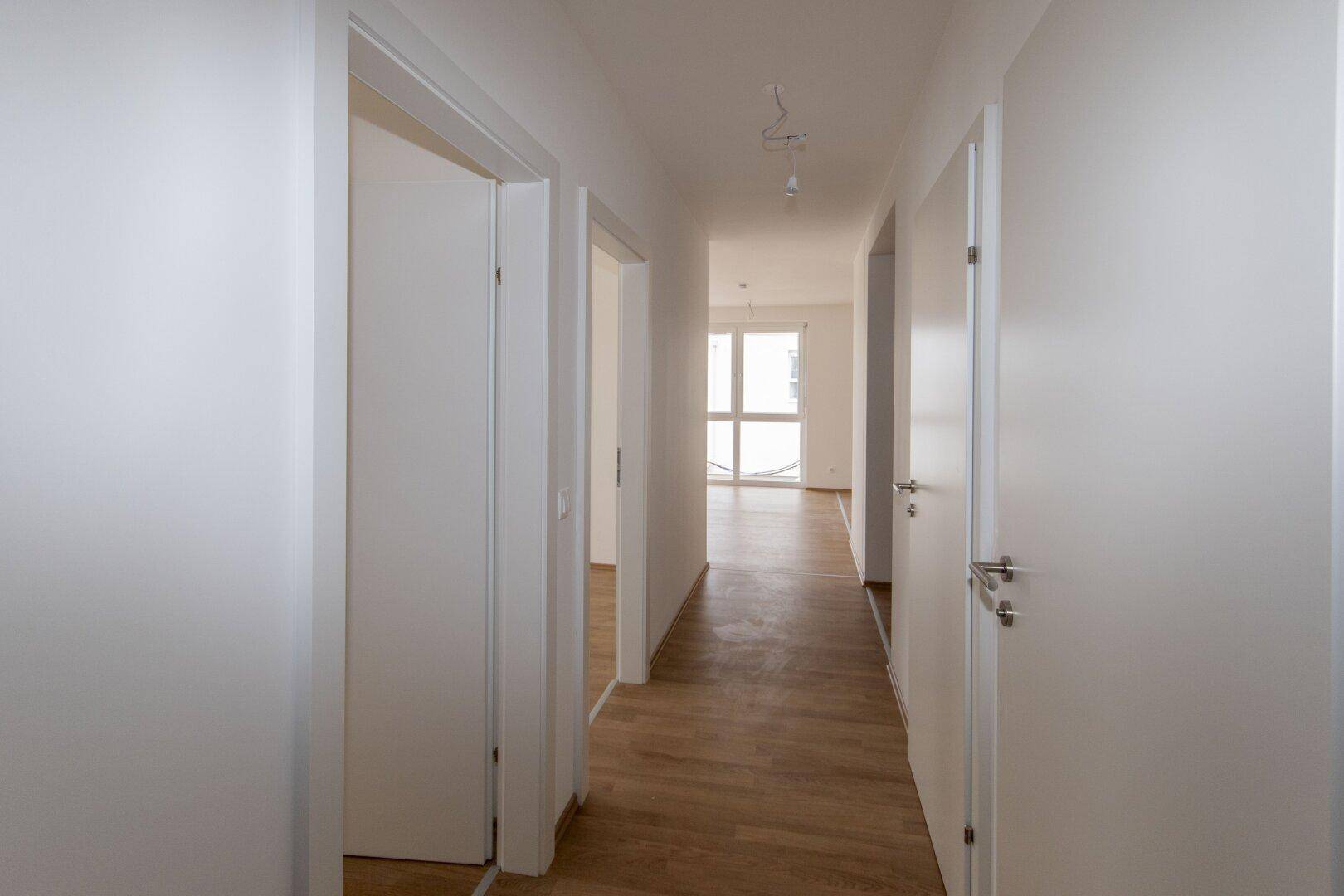 Langer, heller Flur mit mehreren Türen und Laminatboden in einem modernen Neubau.