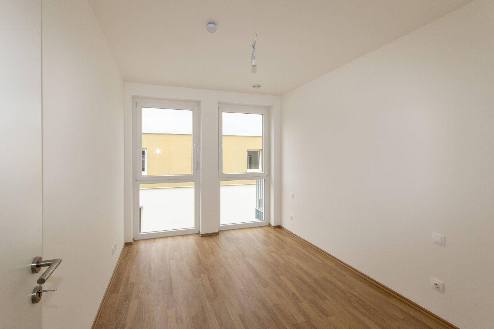 Geräumiges Schlafzimmer mit Laminatboden und zwei Fenstern für optimale Belichtung und Ausblick.