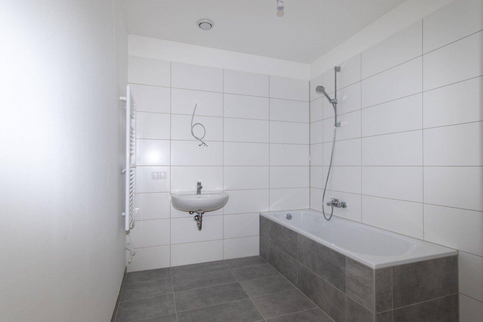 Modernes Badezimmer mit Badewanne, Waschbecken und weißen Wandfliesen sowie einem Handtuchheizkörper.