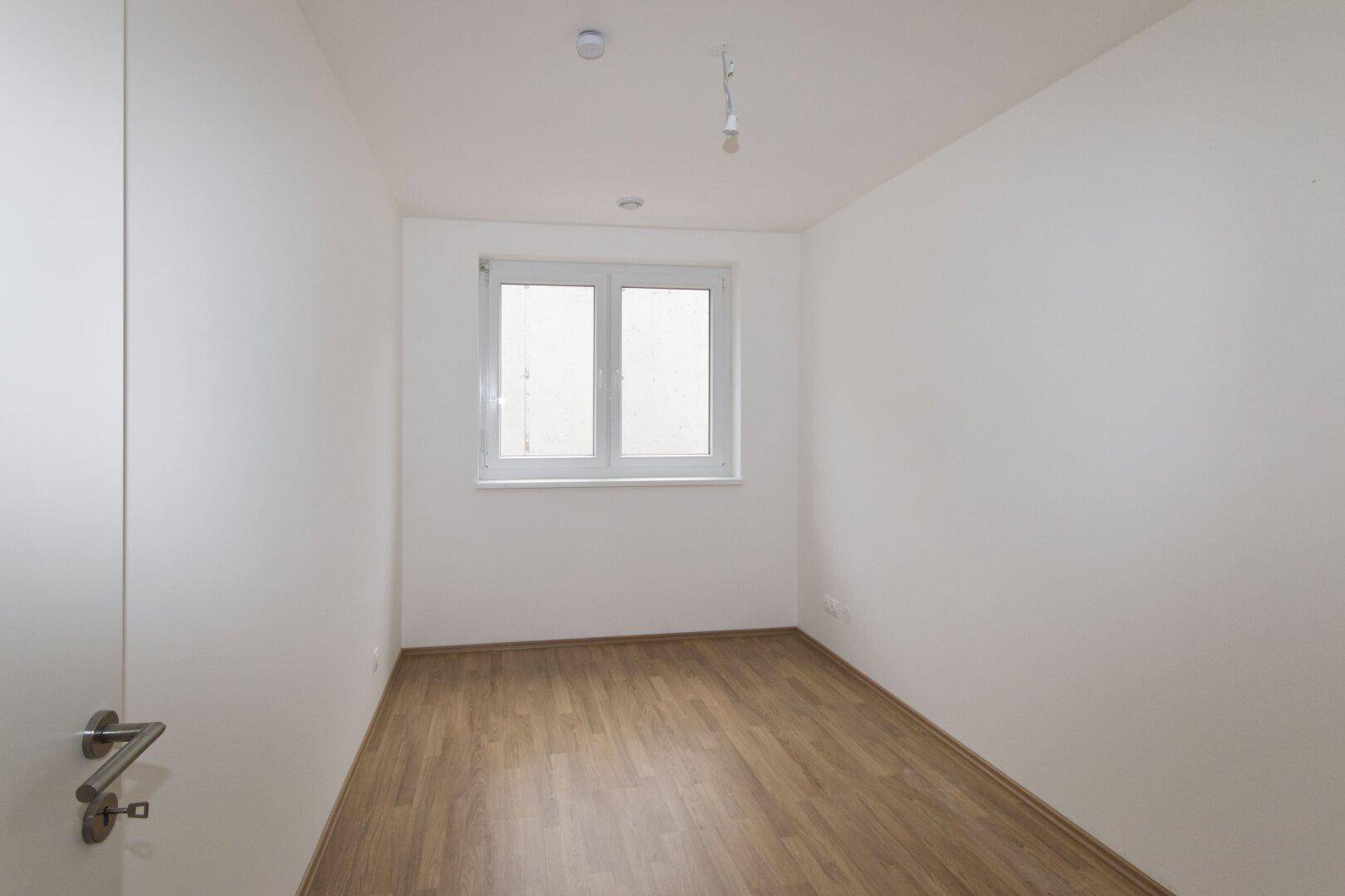 Helles, unmöbliertes Schlafzimmer mit Holzboden und einem Fenster.