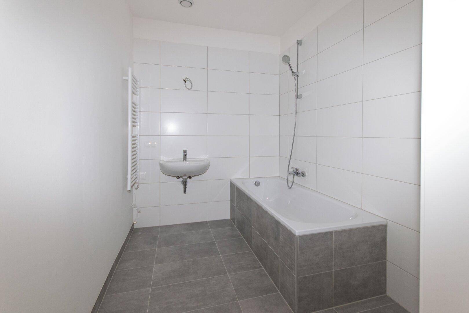 Modernes Badezimmer mit weißen Wandfliesen, grauen Bodenfliesen, Badewanne und Waschbecken.
