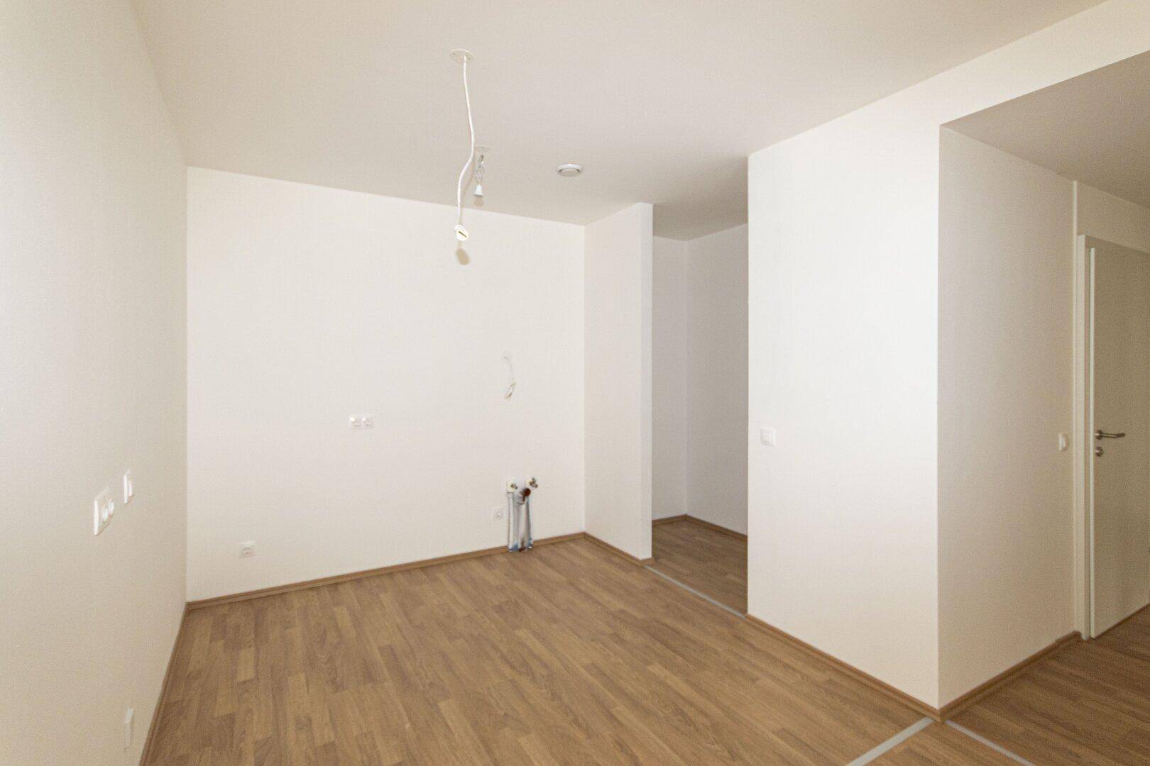 Leerer Küchenbereich mit Anschlüssen für eine Einbauküche und hellem Holzboden.