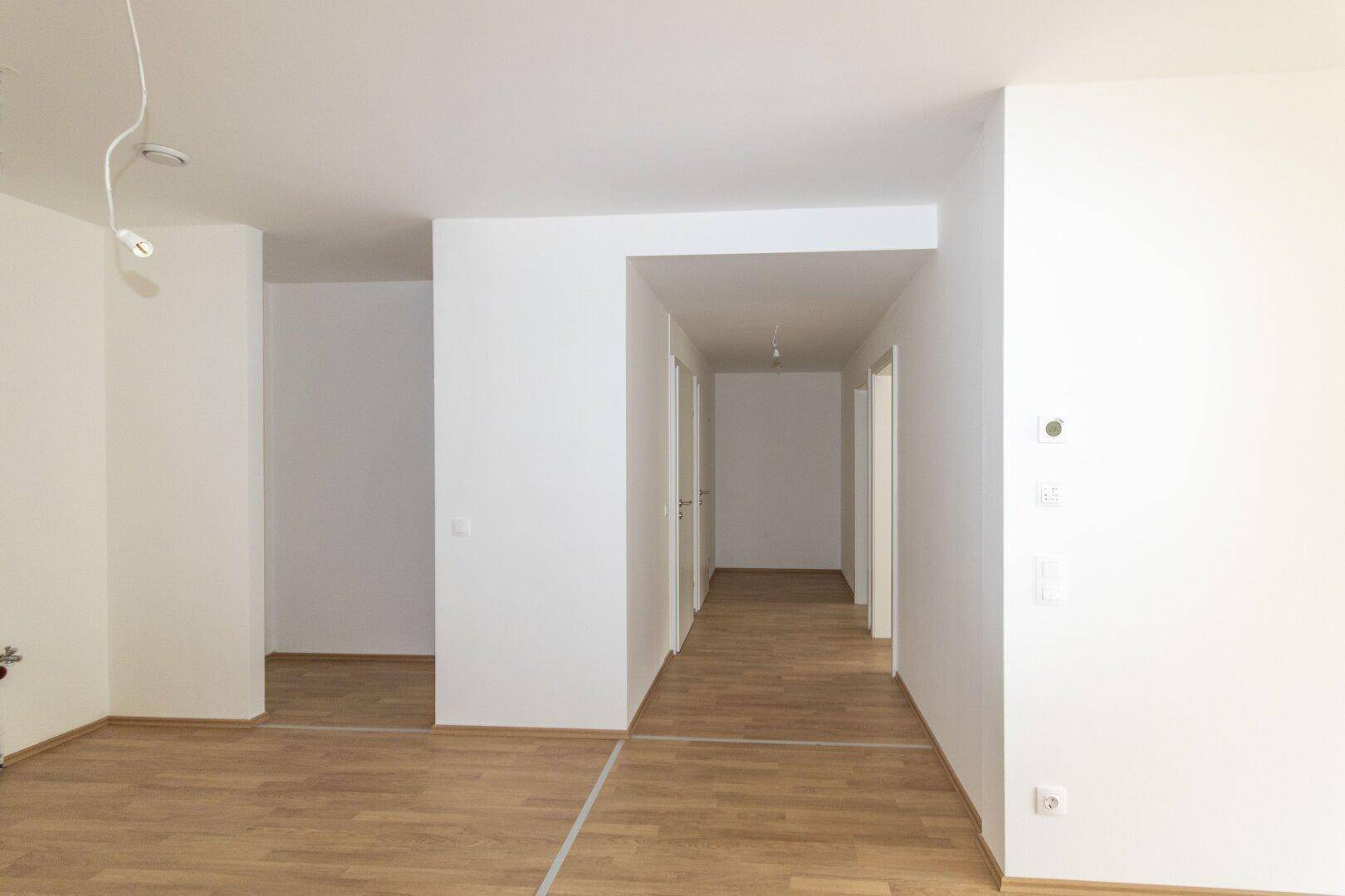 Langer Flur mit hellem Holzboden und mehreren Türen, der zu verschiedenen Räumen führt.