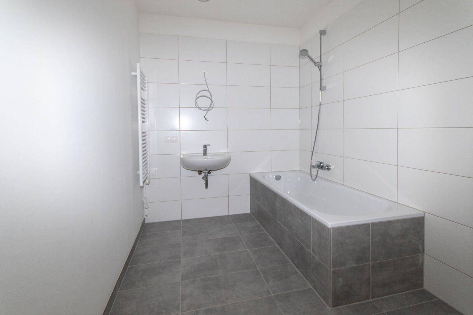 Modernes Badezimmer mit Badewanne, Waschbecken, Handtuchheizkörper und weißen Fliesen.