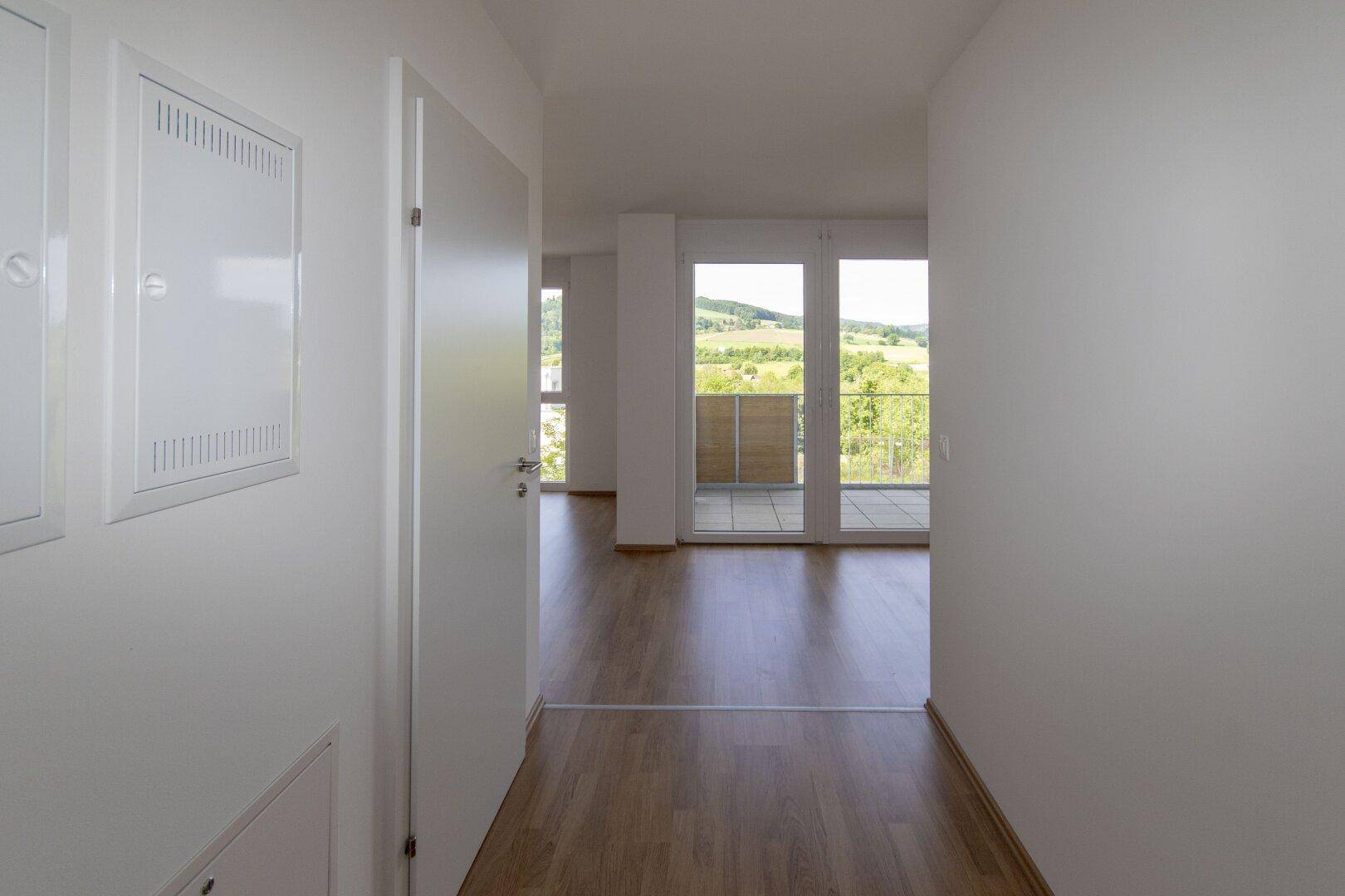 Flur mit Laminatboden und Blick auf einen hellen Raum mit Balkonzugang und Landschaftsblick.