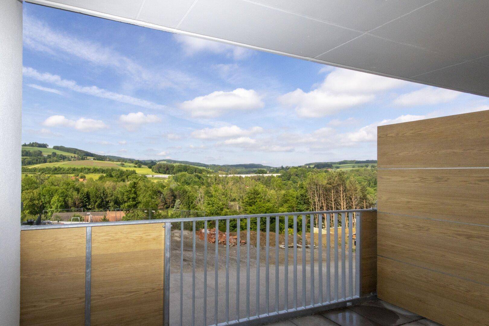 Balkon mit Holzelementen und weitem Ausblick auf die umliegende Natur und Hügel.