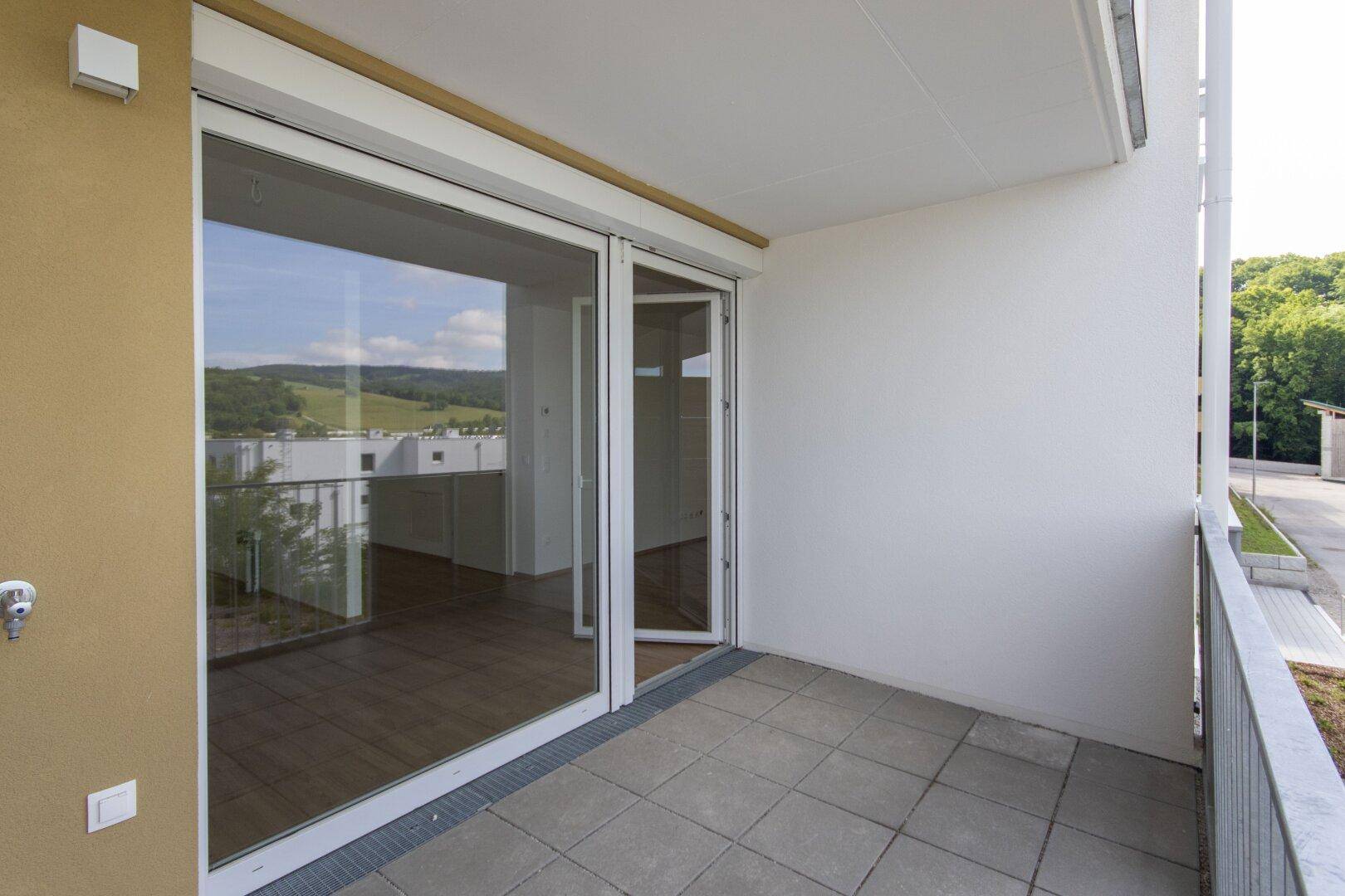 Heller Balkon mit Fliesenboden und Zugang zu den Innenräumen durch große Schiebetüren.