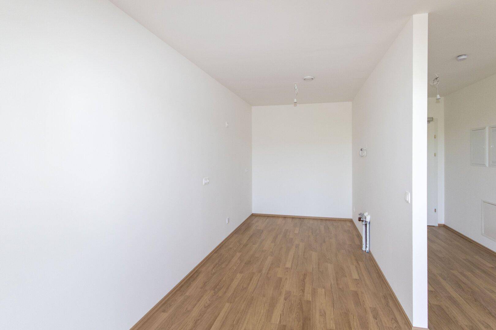 Langer, schmaler Raum mit Laminatboden und weißen Wänden, bereit für die Einrichtung.