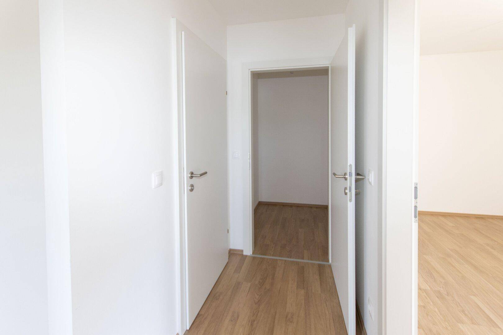 Heller Flur mit mehreren weißen Türen und Laminatboden, der die verschiedenen Räume verbindet.