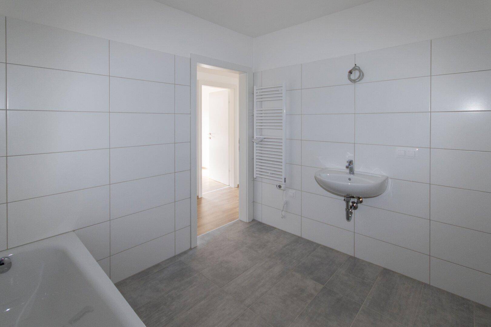 Helles Badezimmer mit Waschbecken, beheiztem Handtuchhalter und weißen Wandfliesen.
