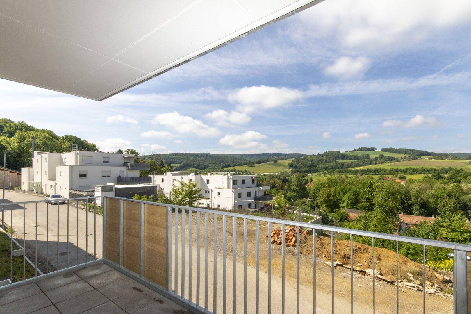 Balkon mit Blick auf die umliegenden Neubauten und die hügelige, grüne Landschaft.