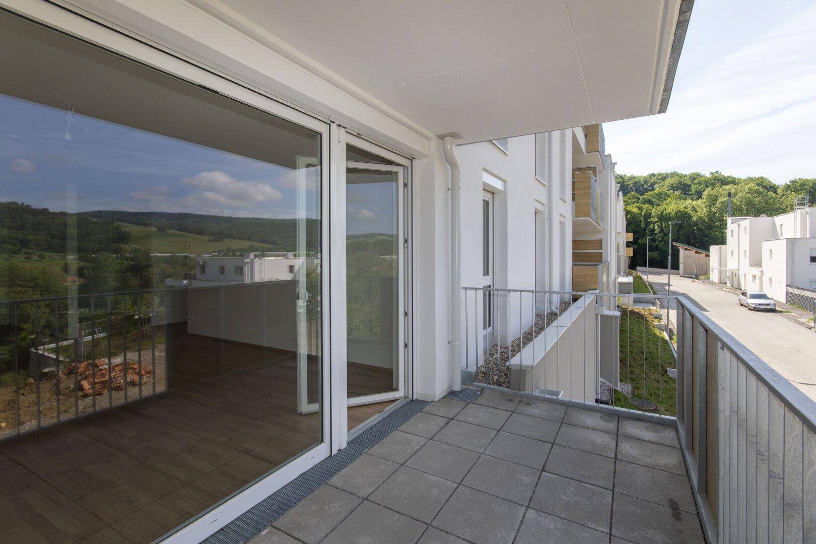 Heller Balkon mit Fliesenboden und Zugang zu einem modernen Wohnbereich mit großen Fenstern.
