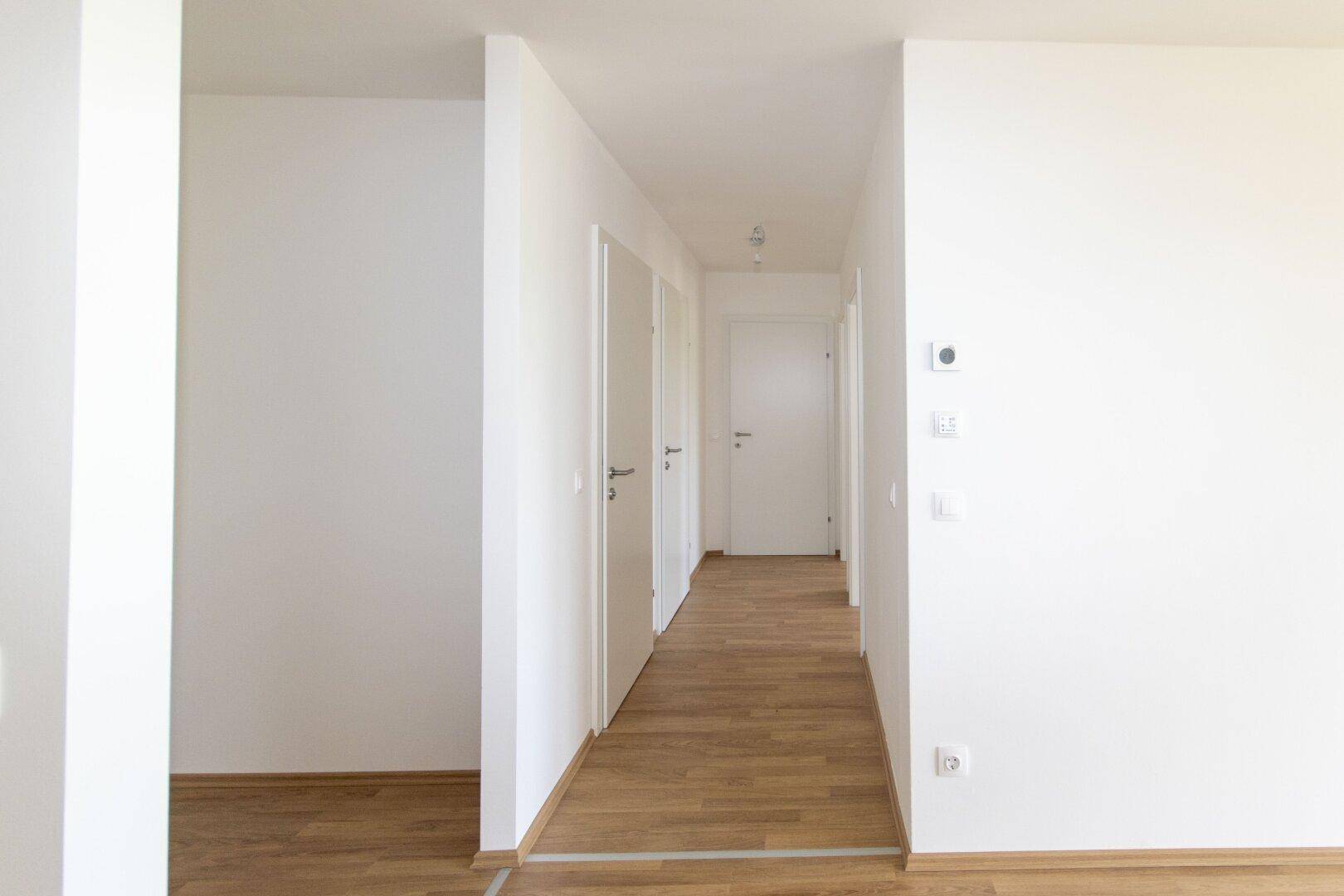 Langer, heller Flur mit Holzboden und mehreren weißen Türen, die zu den Zimmern führen.