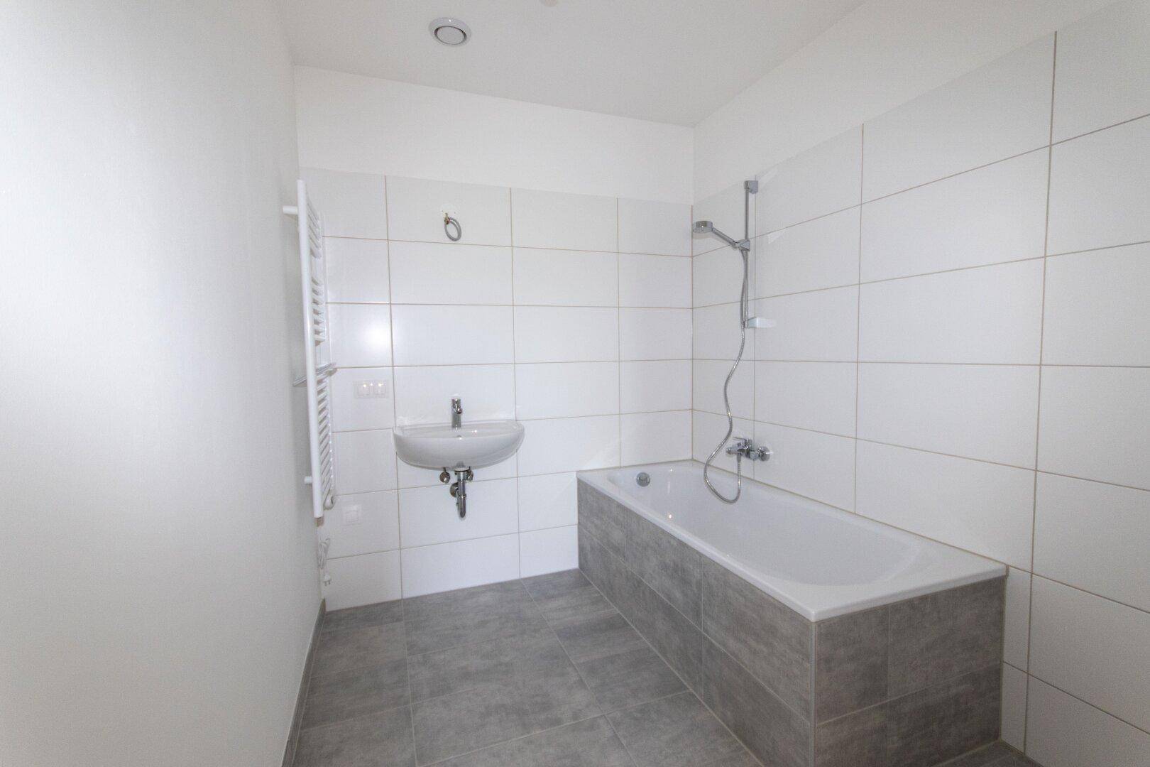 Modernes Badezimmer mit weißen Fliesen, Badewanne und Waschbecken, ausgestattet mit Handtuchheizkörper.