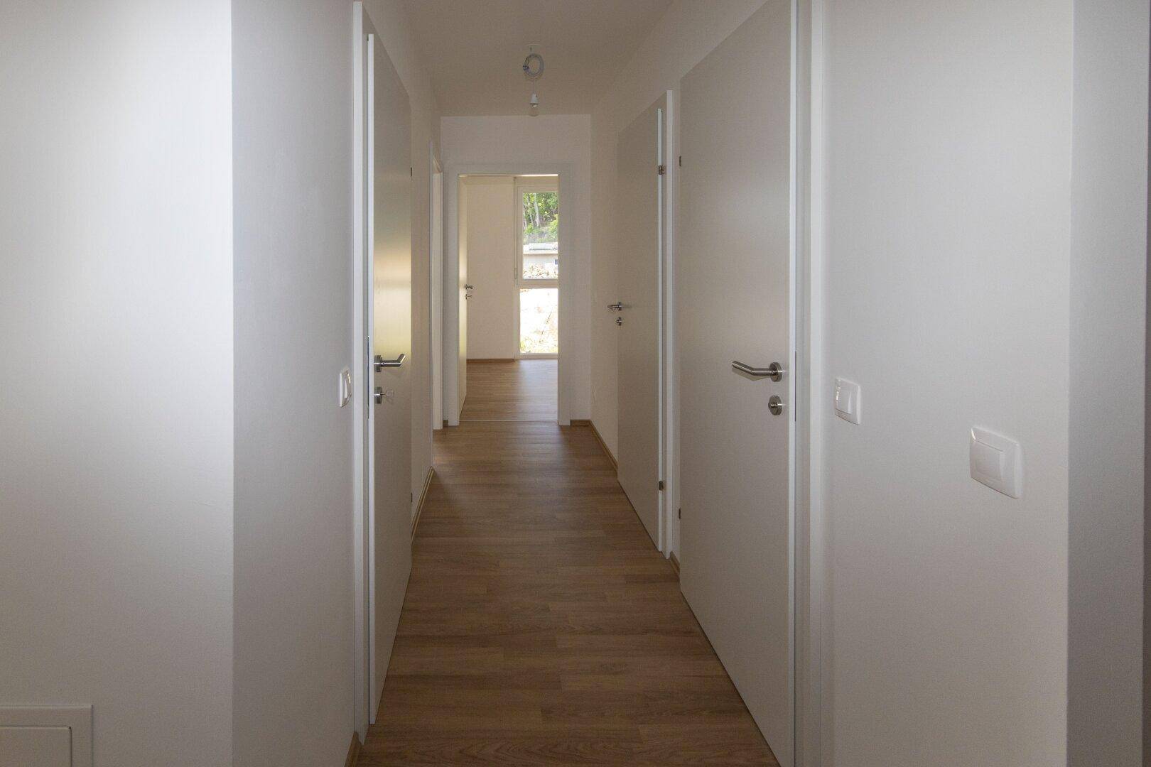 Langer, heller Flur mit Laminatboden, der zu den verschiedenen Zimmern der Wohnung führt.