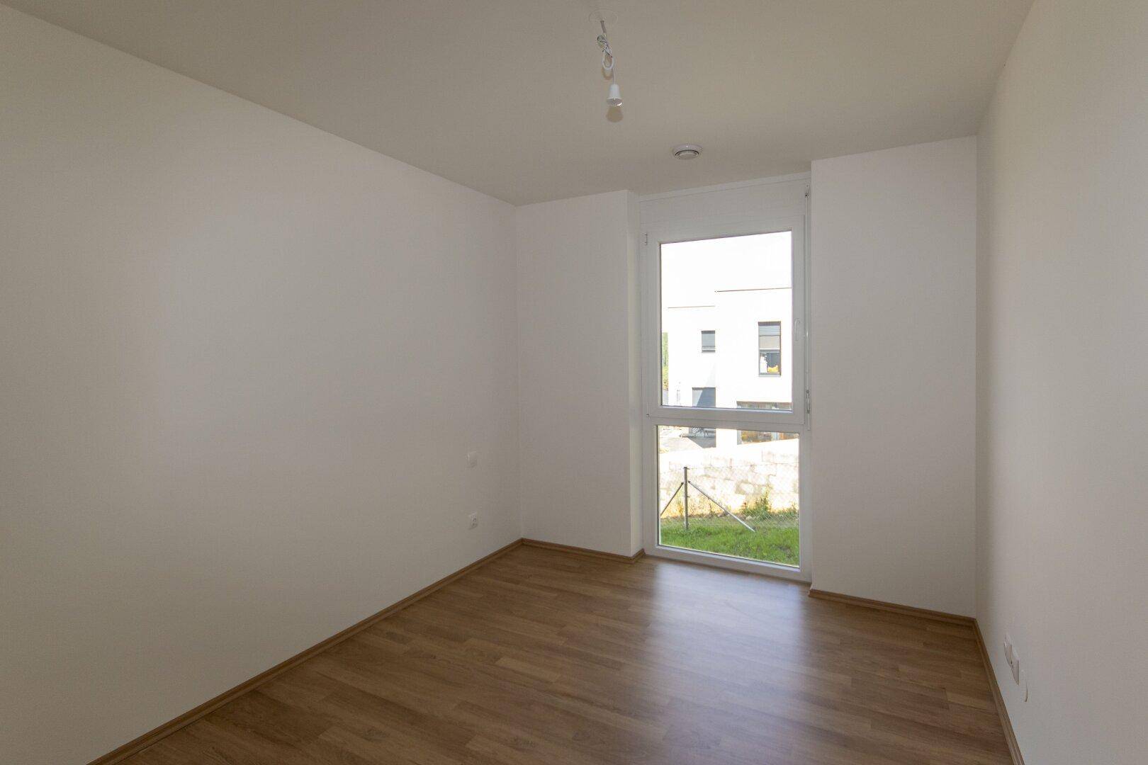 Schlafzimmer mit Laminatboden und Fenster, das einen Blick auf die umliegenden Gebäude bietet.