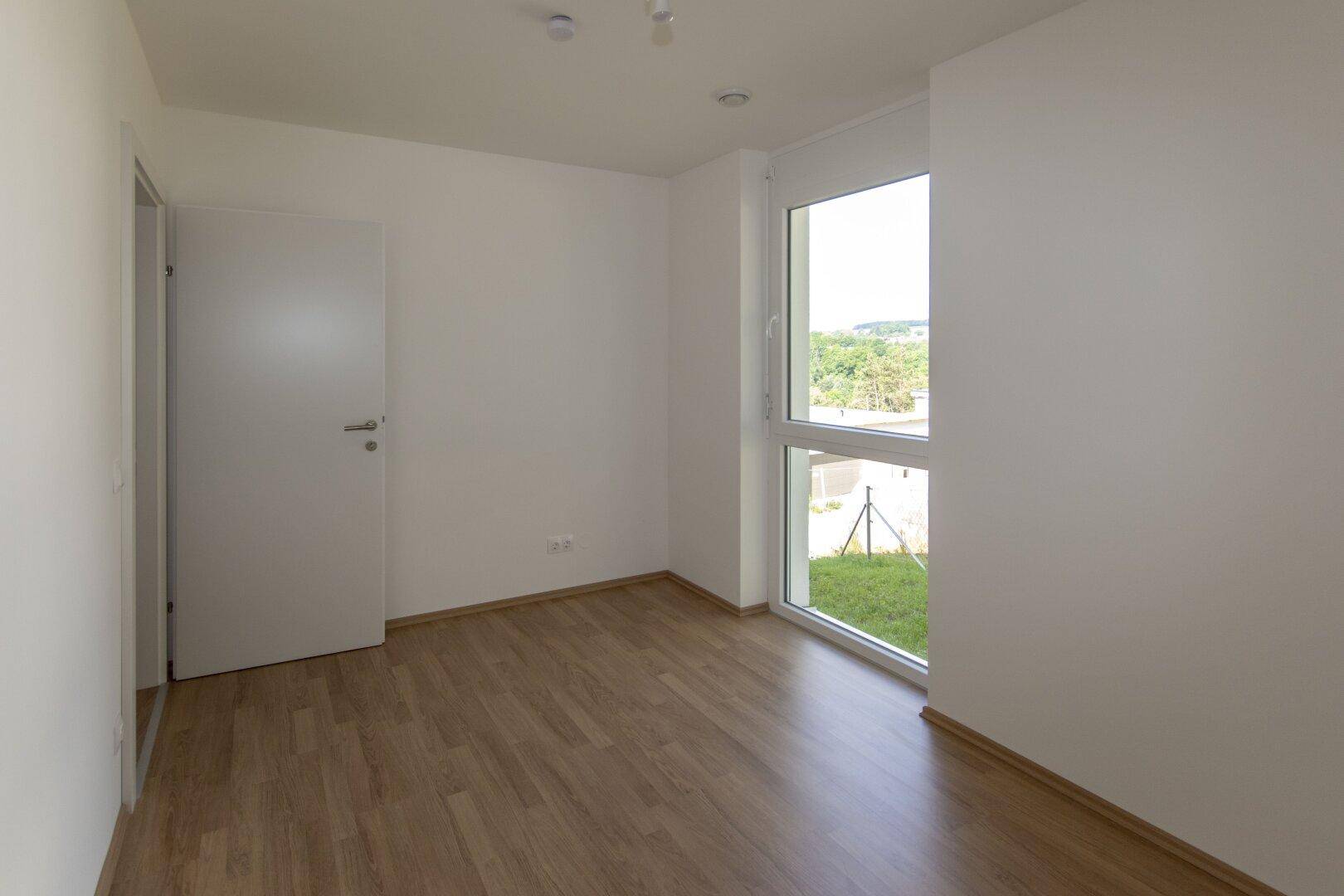 Geräumiges Schlafzimmer mit Laminatboden und viel Tageslicht durch das große Fenster.
