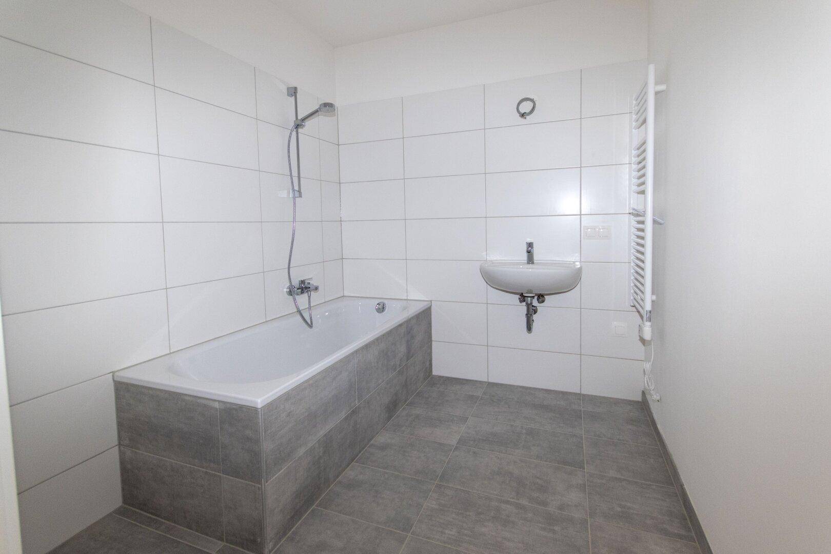 Modernes Badezimmer mit Badewanne, Waschbecken, weißen Wandfliesen und grauem Boden.