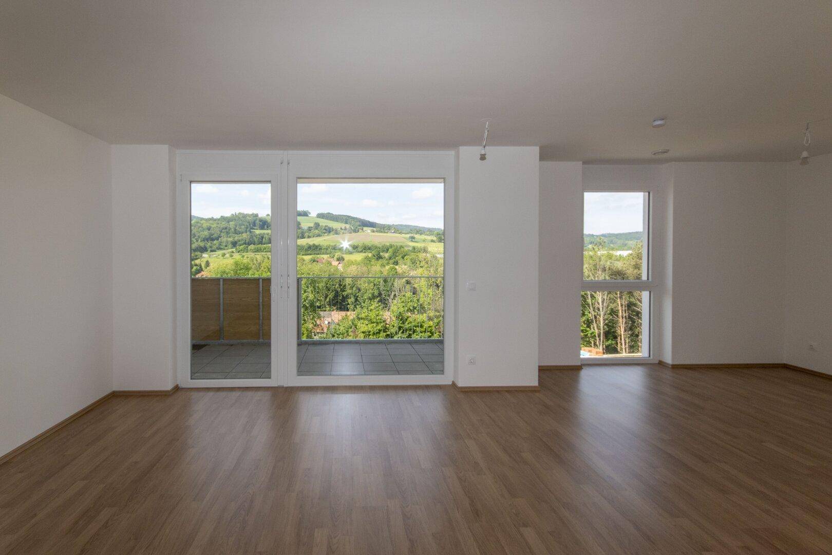 Modernes Wohnzimmer mit hellem Laminatboden und Panoramafenstern mit Blick auf die Natur.