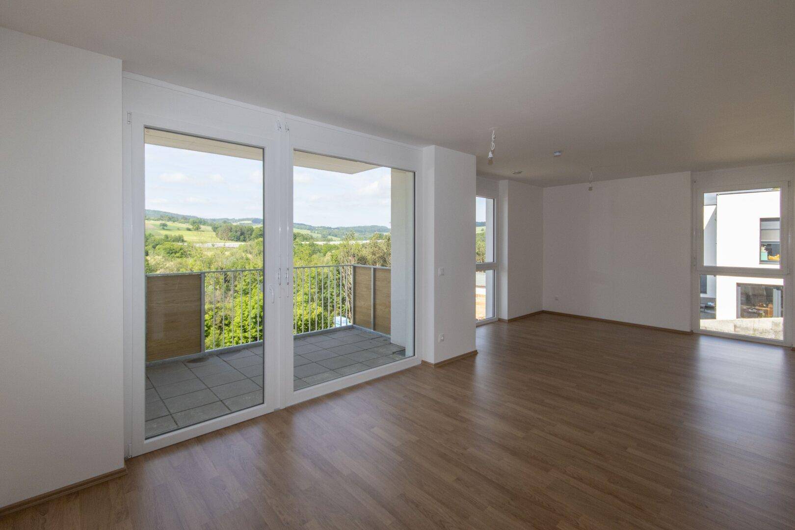 Geräumiges Wohnzimmer mit großen Fenstern, die viel Tageslicht hereinlassen und einen Balkonzugang bieten.