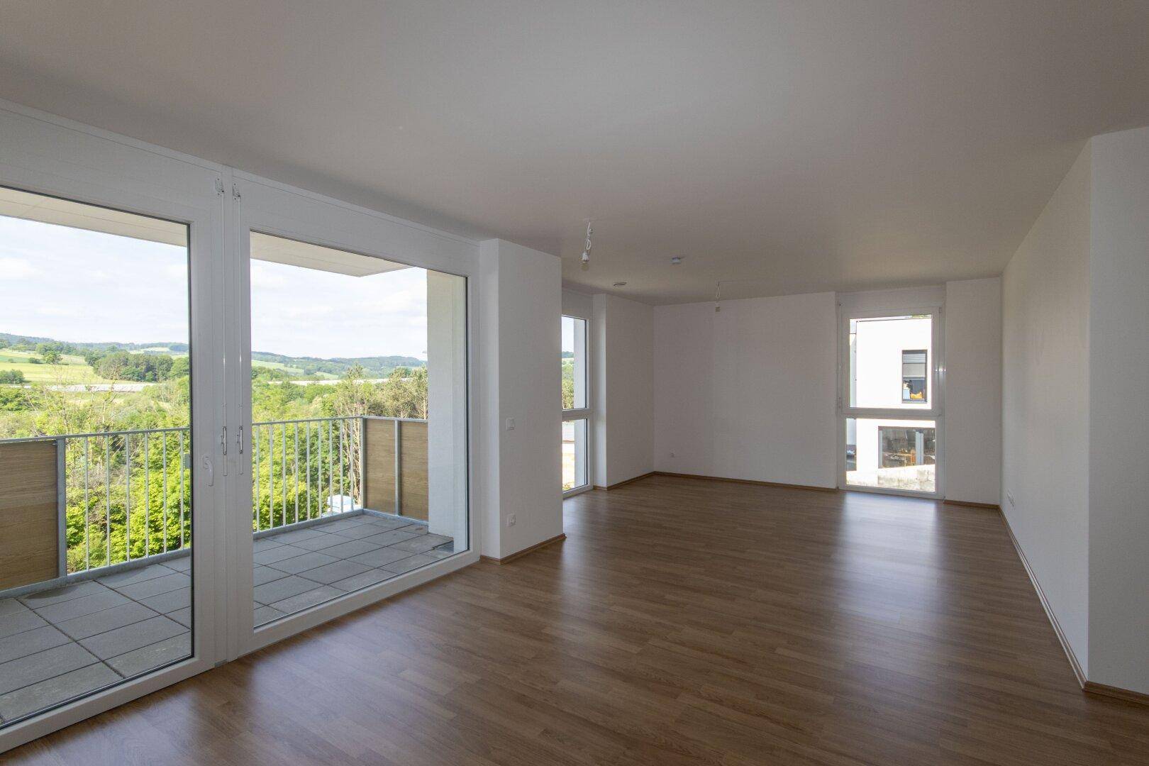 Lichtdurchflutetes Wohnzimmer mit Zugang zum Balkon und weitem Blick über die Landschaft.