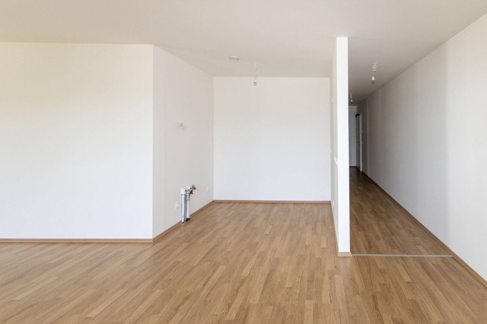 Leerer Küchenbereich mit vorbereiteten Anschlüssen und hellem Laminatboden.