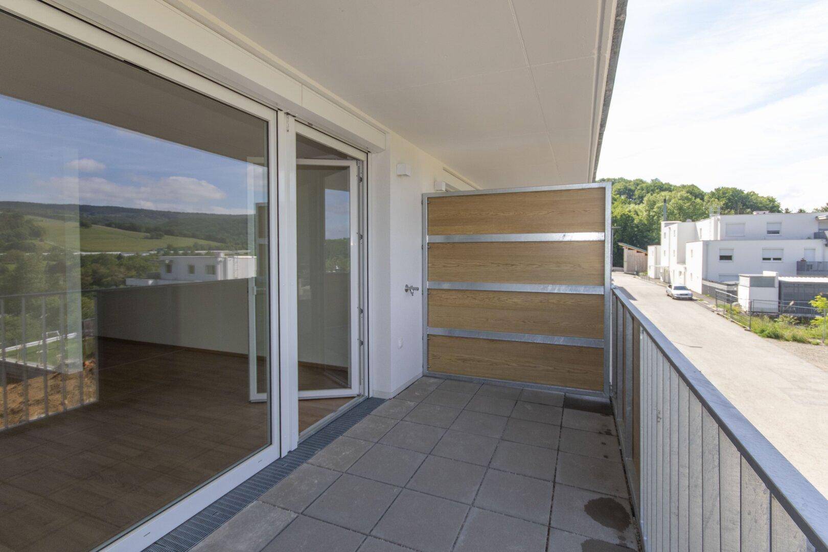 Heller Balkon mit großen Schiebetüren und Zugang zu den Innenräumen, umgeben von Natur.