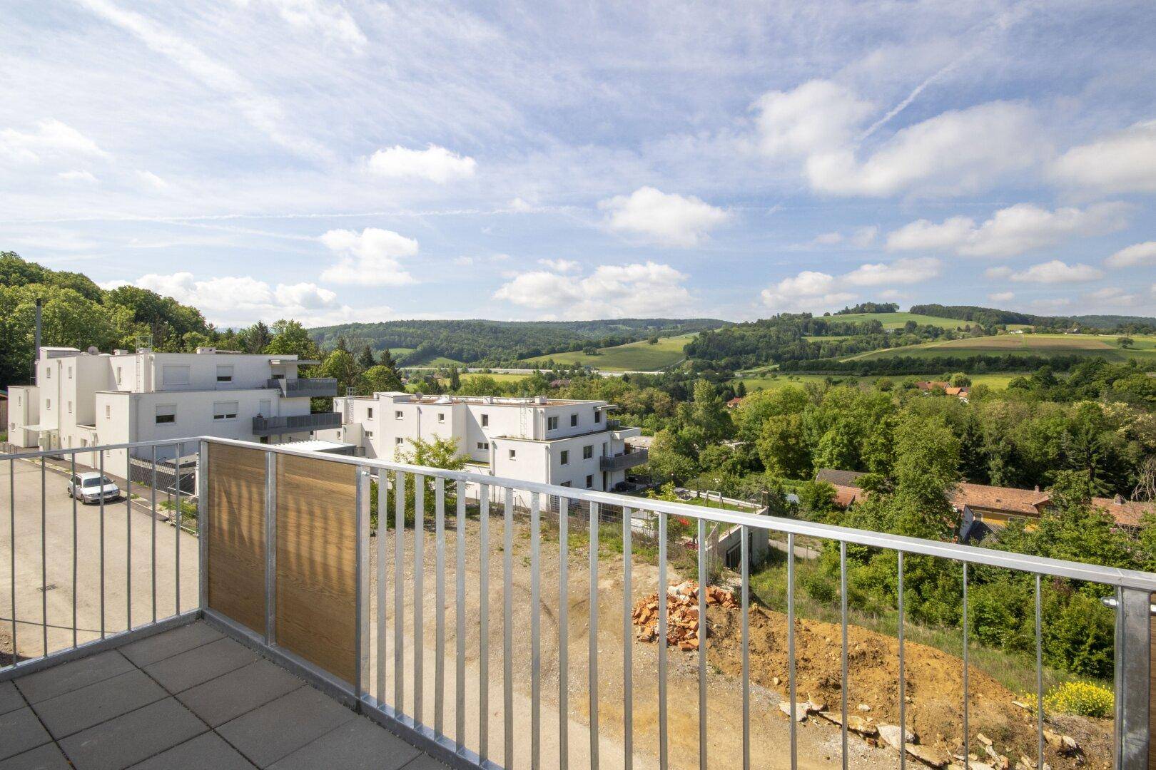 Balkon mit Blick auf moderne Gebäude, eine Straße und die umliegende hügelige Landschaft.