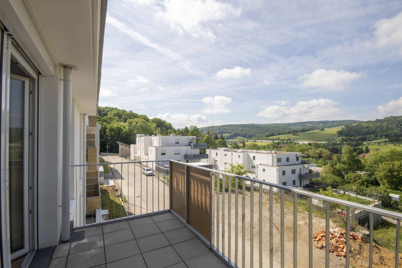 Heller Balkon mit Fliesenboden und weitem Ausblick auf die moderne Wohnanlage und Natur.