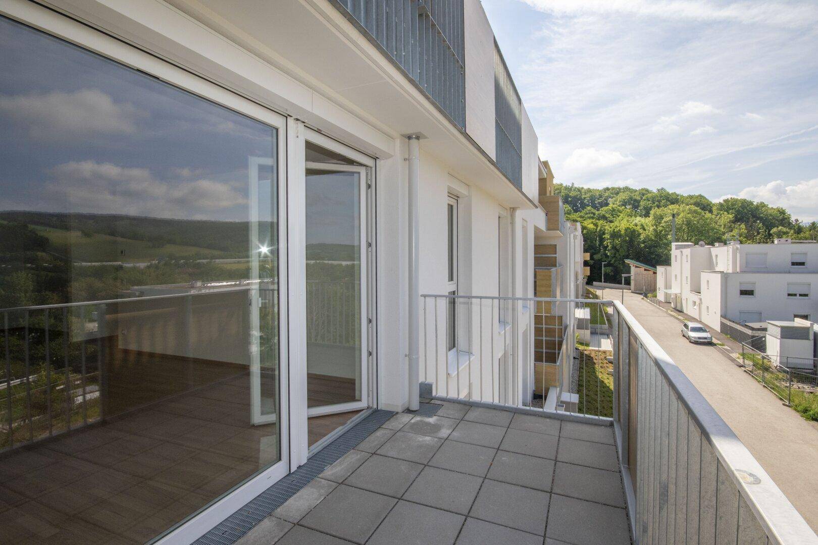 Balkon mit großen Schiebetüren zum Innenbereich und Blick auf die Umgebung und grüne Hügel.