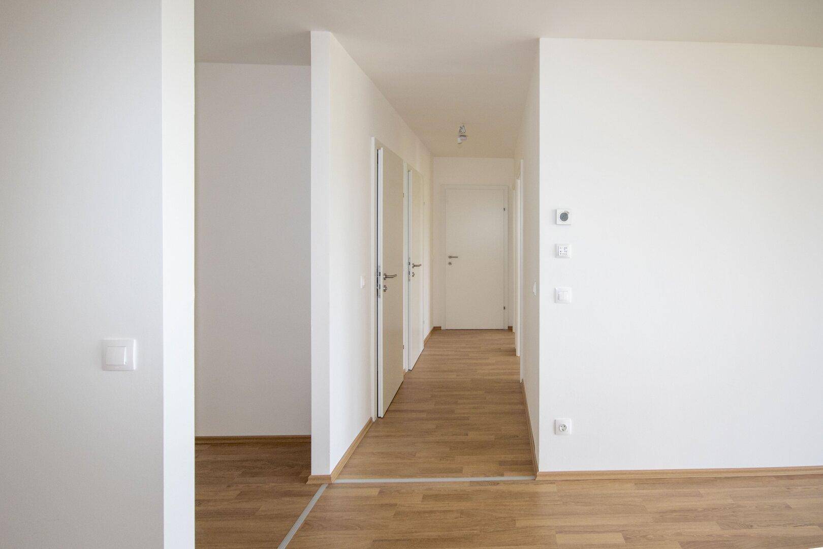 Eingangsbereich mit hellem Laminatboden und mehreren weißen Türen, die zu den Zimmern führen.